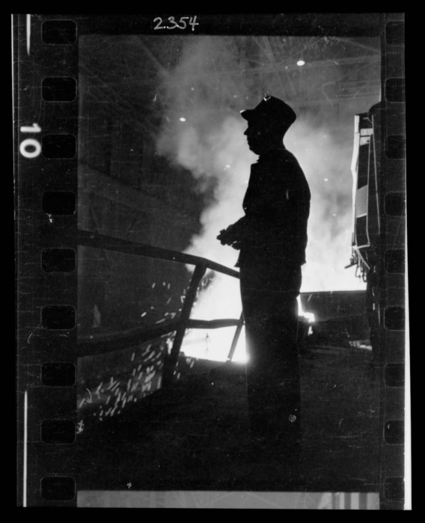 Steel worker standing in mill with smelter in the background, in Chicago, Illinois