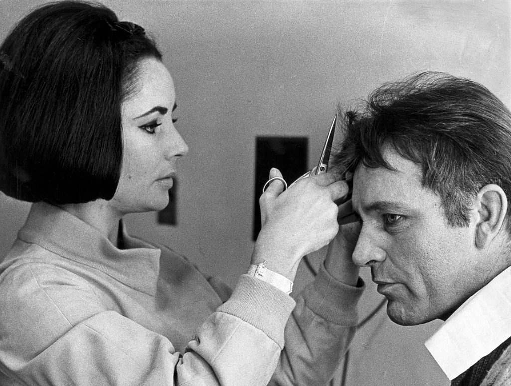 6th March 1964: Elizabeth Taylor gives her future husband Richard Burton (1925-1984) a cursory haircut with a pair of scissors. (Photo by William Lovelace/Express/Getty Images)