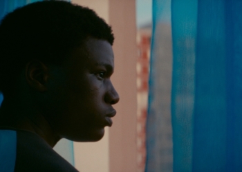 bir erkek perdelerin arkasından camdan dışarıya bakıyor.