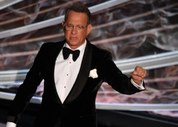 smokinli bir adam ödül töreninde konuşma yapıyor.