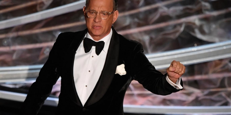 smokinli bir adam ödül töreninde konuşma yapıyor.